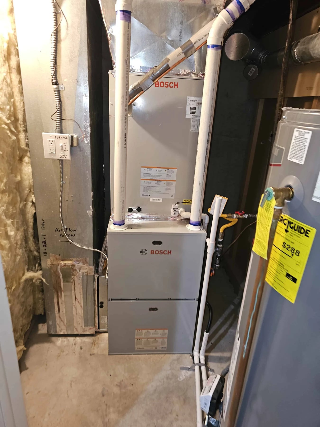 Bosch furnace with a coil cabinet on top and white PVC vent pipes, a water heater beside it