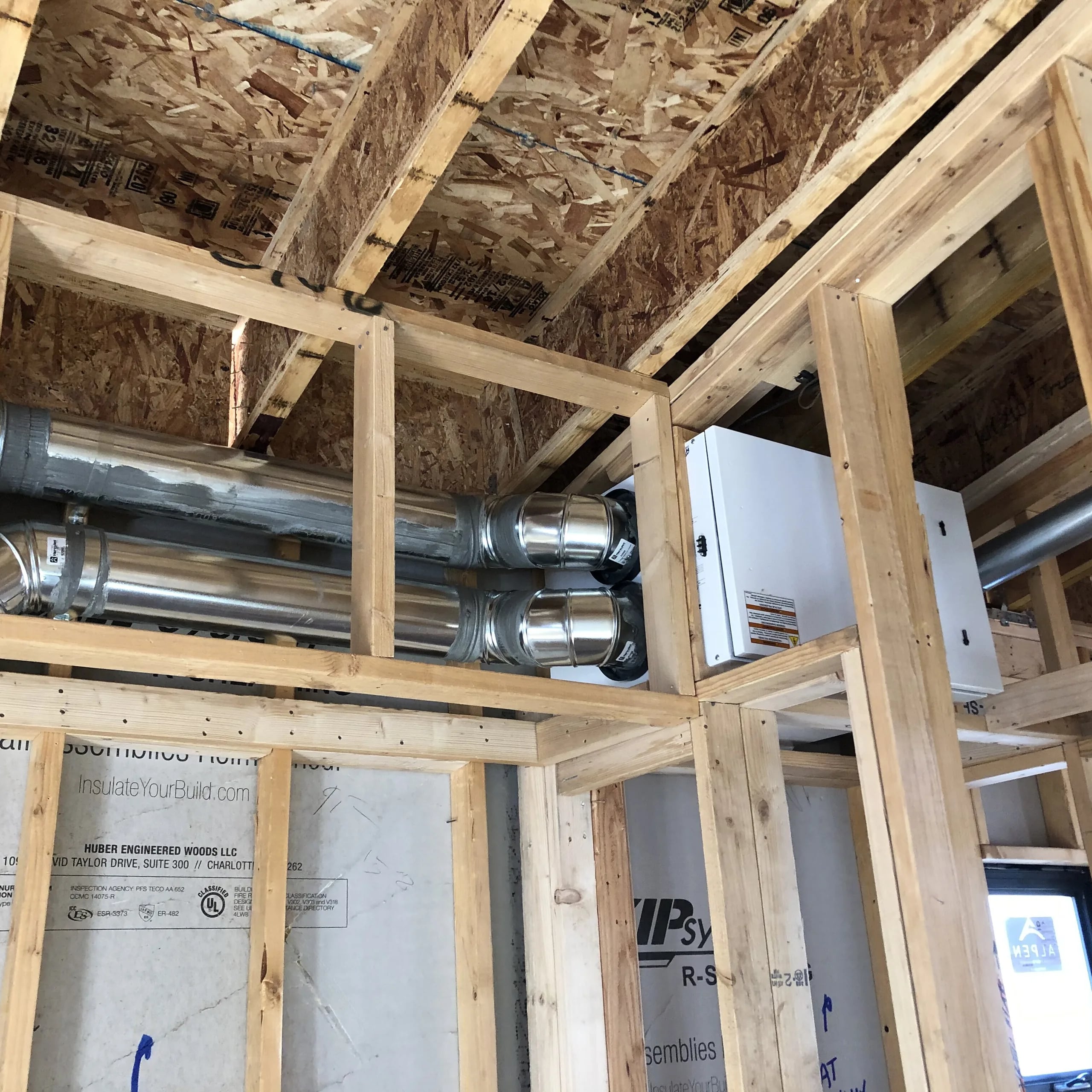 Metal ducts running through open wood framing to a wall-mounted unit