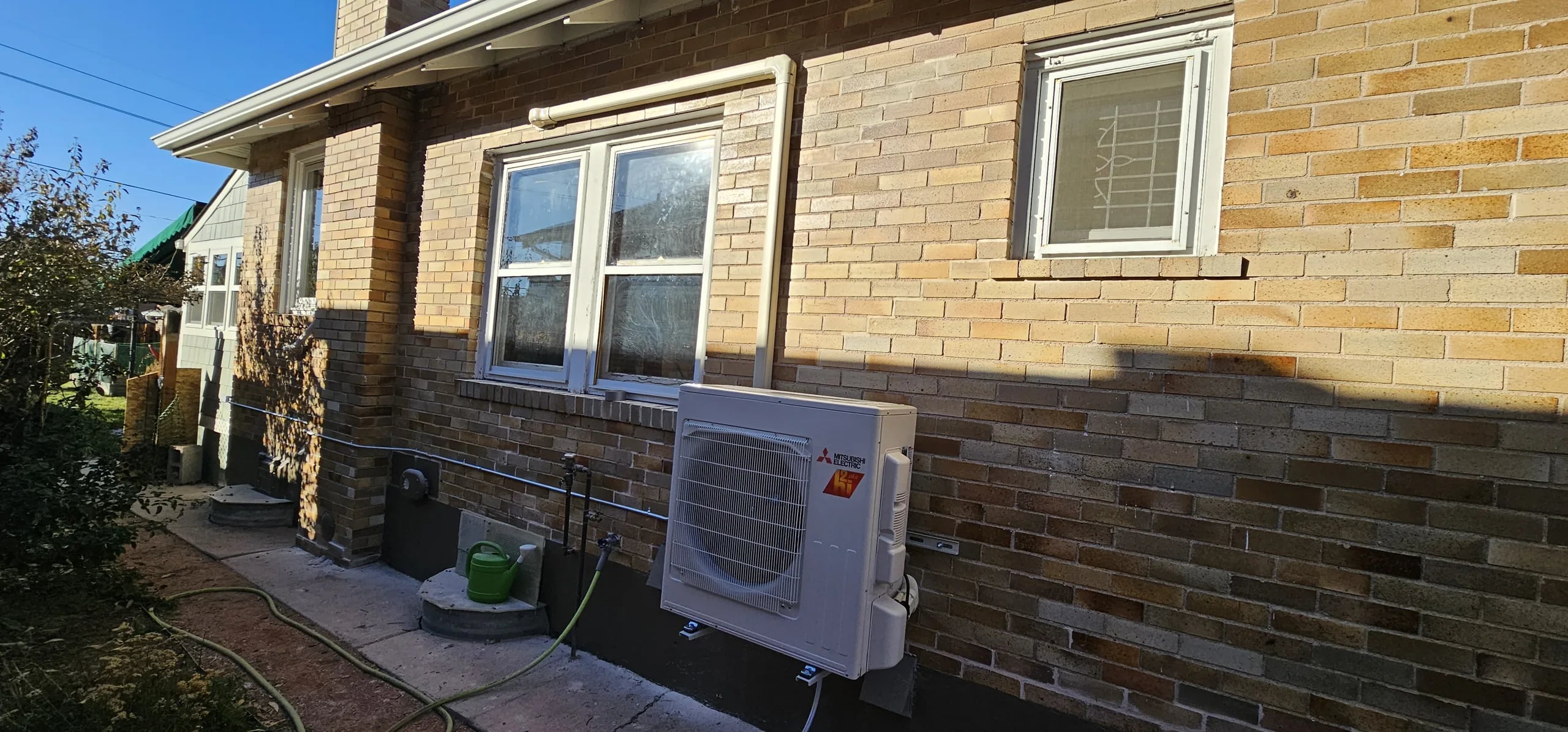 Mitsubishi outdoor unit mounted on a yellow brick wall below a window