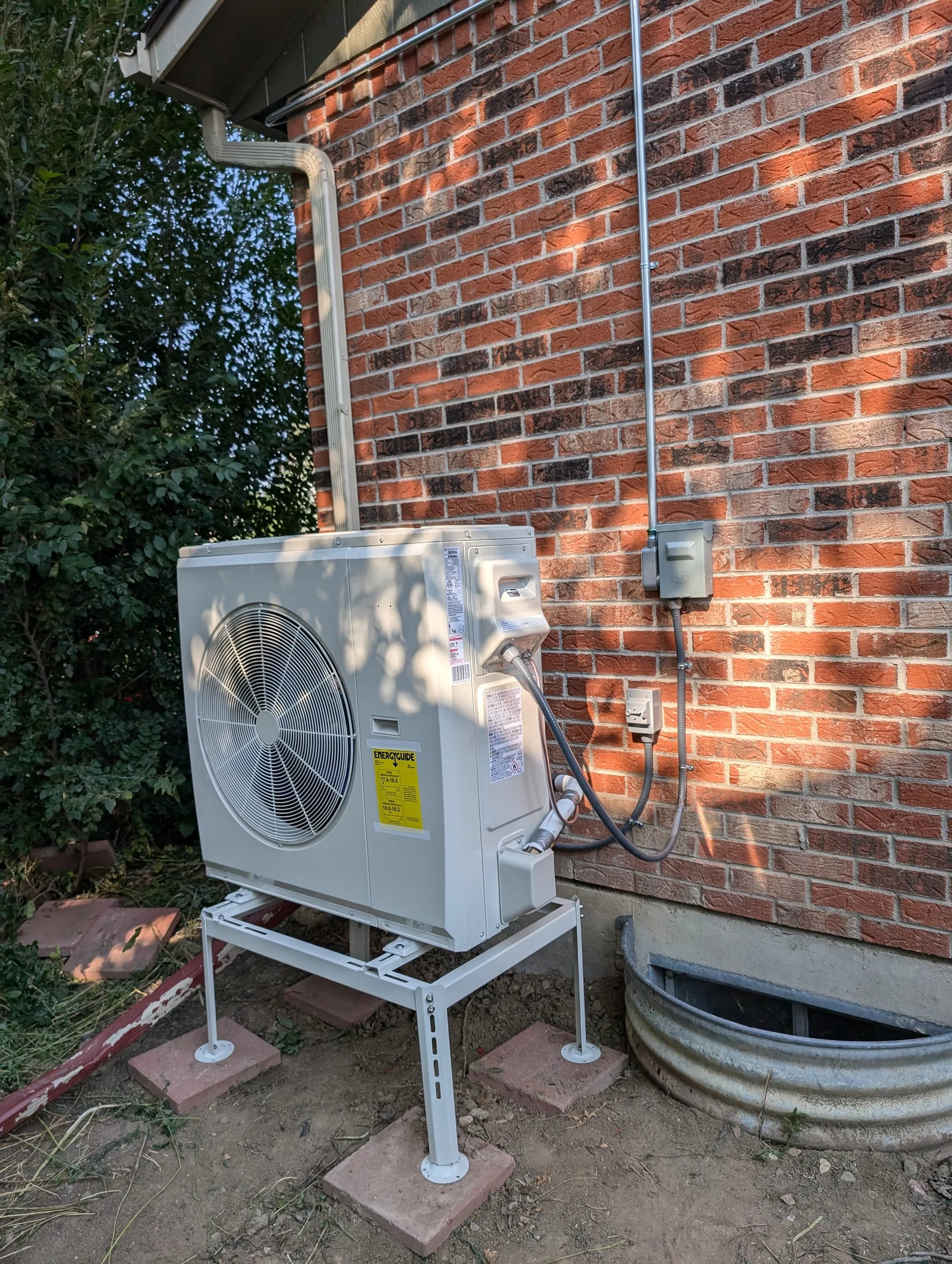 Outdoor unit on a white steel stand beside a red brick wall and a window well