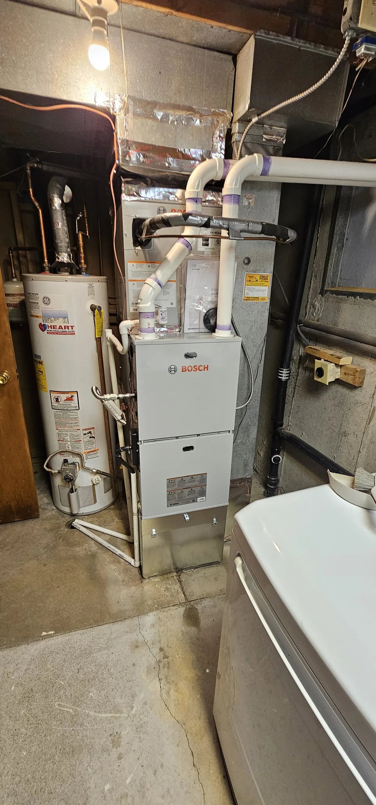 Bosch furnace with white PVC venting beside a water heater in a basement laundry corner