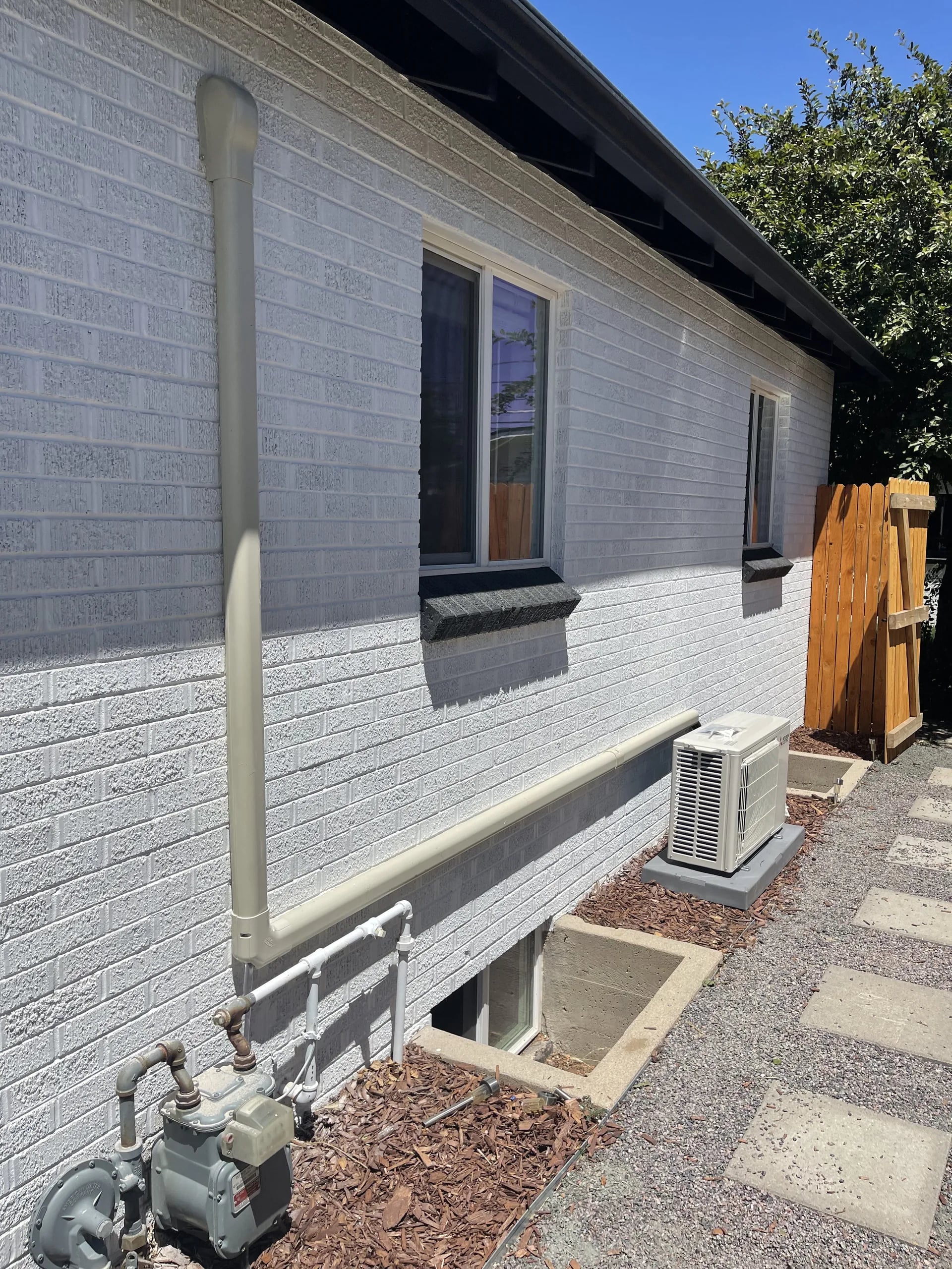 Outdoor unit along a painted gray brick house with a white line-set cover running down the wall