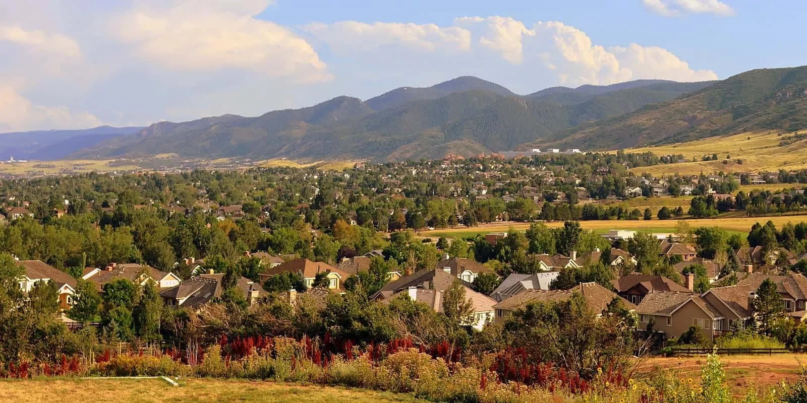 Suburban rooftops among trees below the Front Range foothills