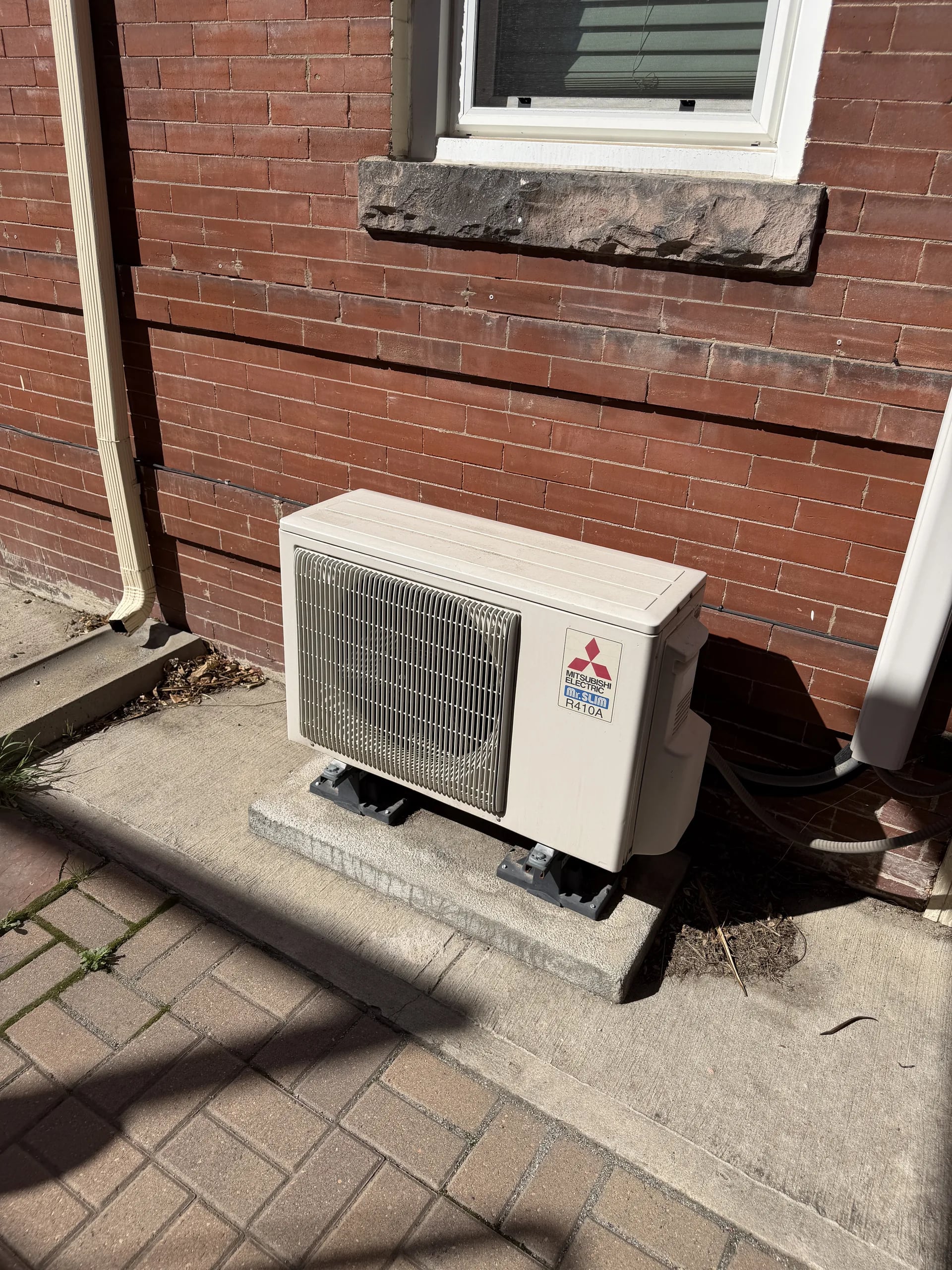 Mitsubishi compact outdoor unit on a pad beside a red brick wall